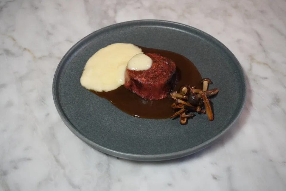 Filete vegetal con demi-glace, espuma de beurre blanc y aros de cebolla en un plato gris, visto desde arriba sobre mármol: la foto de partida.