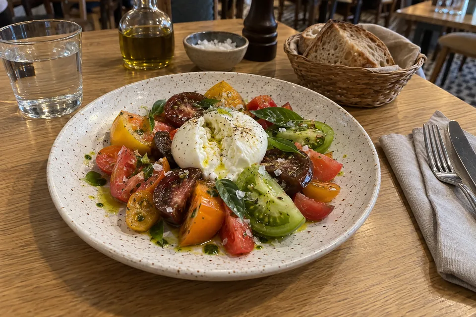 Tomates de colores con burrata y aceite de albahaca en una mesa de restaurante: foto de partida de ejemplo, generada con inteligencia artificial.